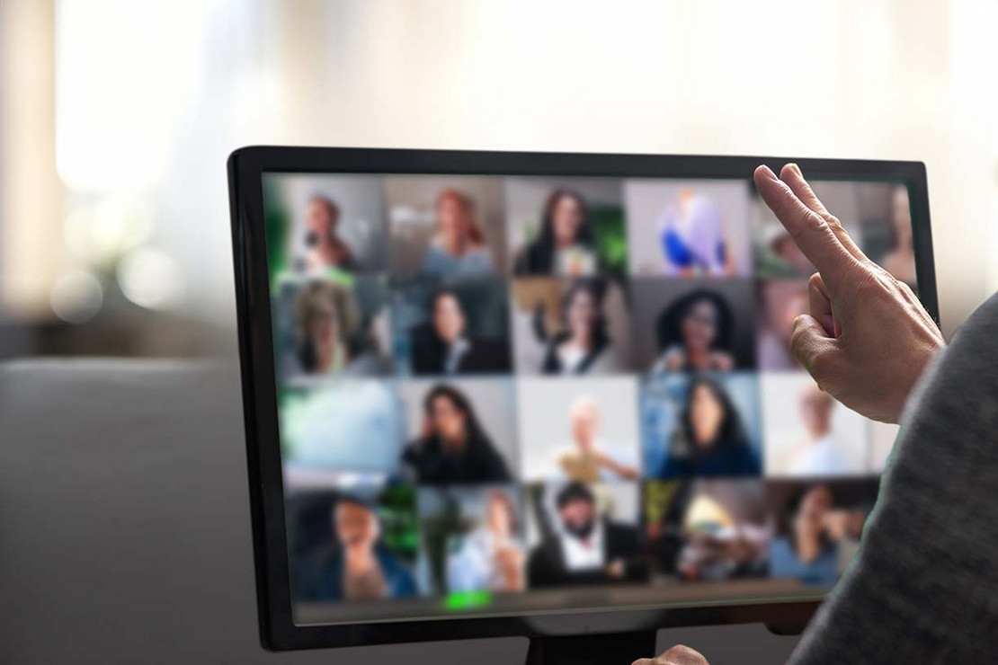 Ein Mensch nimmt an einer digitalen Veranstaltung teil. Auf einem Laptop sind viele Gesichter der Teilnehmenden.