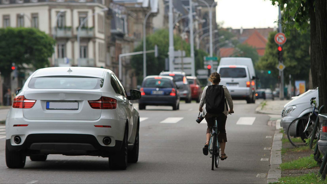 Fahradfahrerin neben einem Luxusauto auf der Straße. 