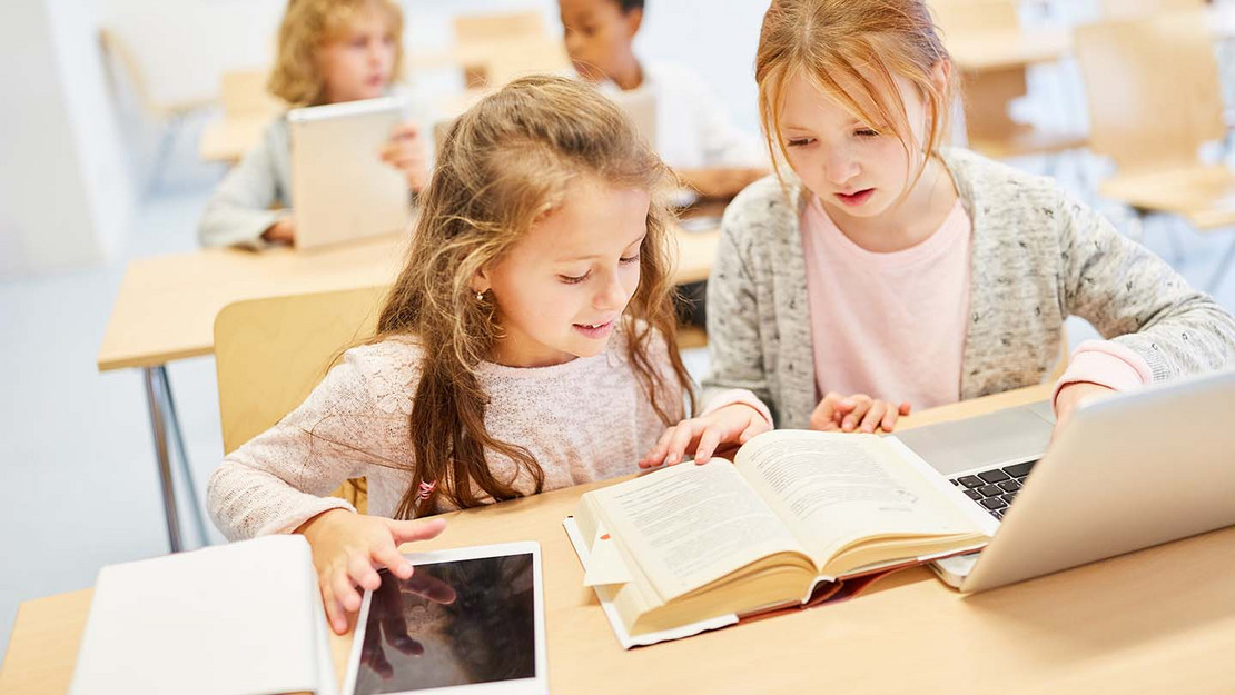 Zwei junge Mädchen in der Schule mit Tablet, Buch und Laptop. 