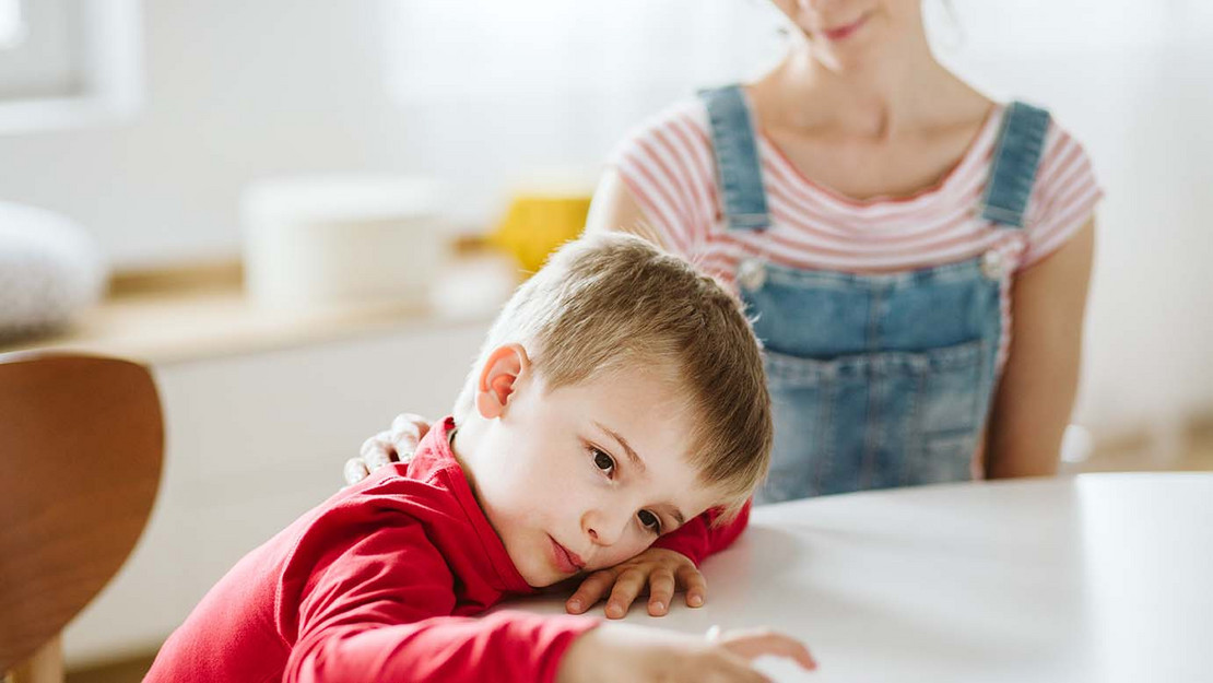 Ein autistisches Kind sitzt an einem Tisch, neben ihm eine Betreuerin.