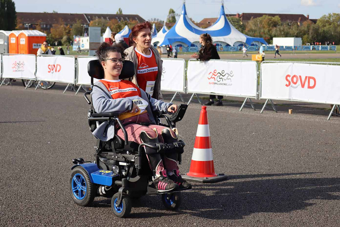 Frau fährt mit einem Elektrorollstuhl an einer Pylone vorbei. 